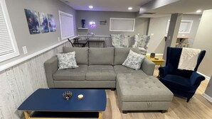 Una sala de estar con un sofá seccional gris, una mesa de centro azul y un sillón azul oscuro.