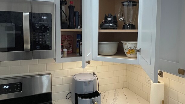 Una cocina compacta con armarios blancos, un microondas, una estufa y una licuadora integrada.
