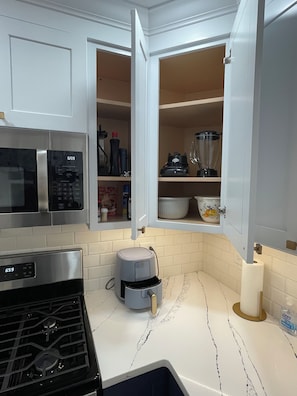 A compact kitchen with white cabinets, a microwave, a stove, and a built-in blender.