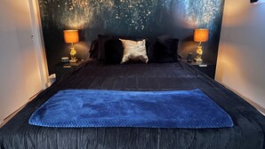Una cama bien hecha con una manta azul, dos lámparas de noche y una pared texturizada detrás de la cama.