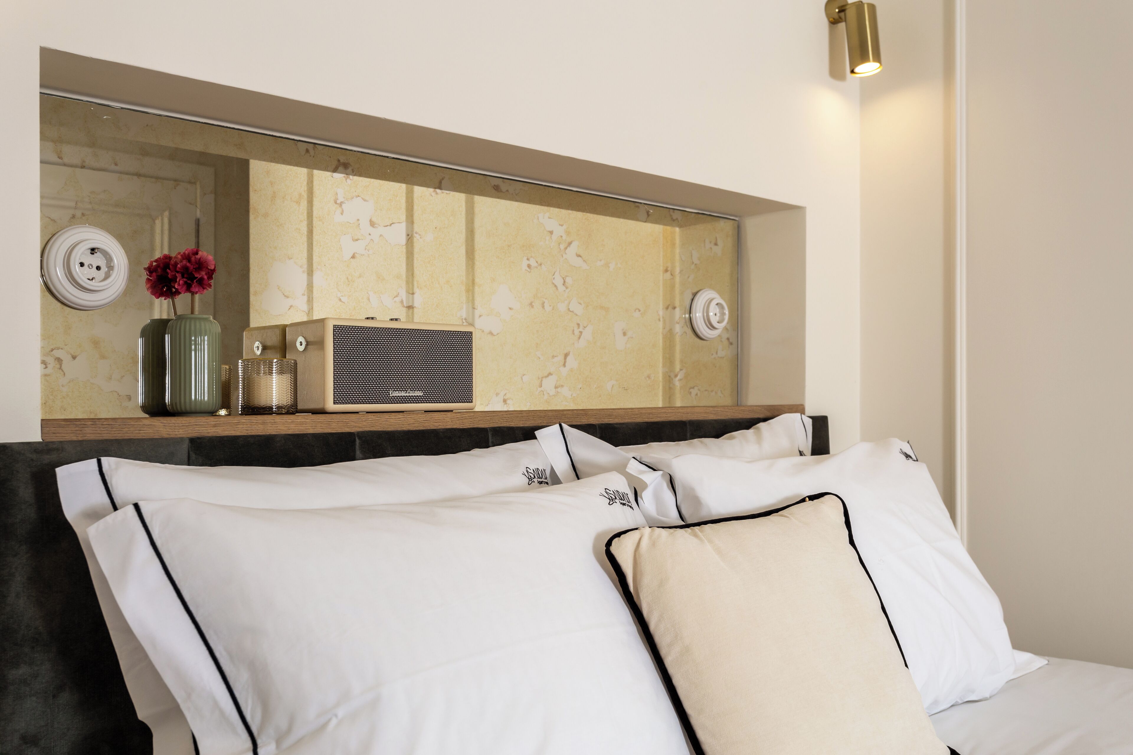 A neatly arranged hotel room with a bed, pillows, a bedside table with a radio, and a mirror above the bed.