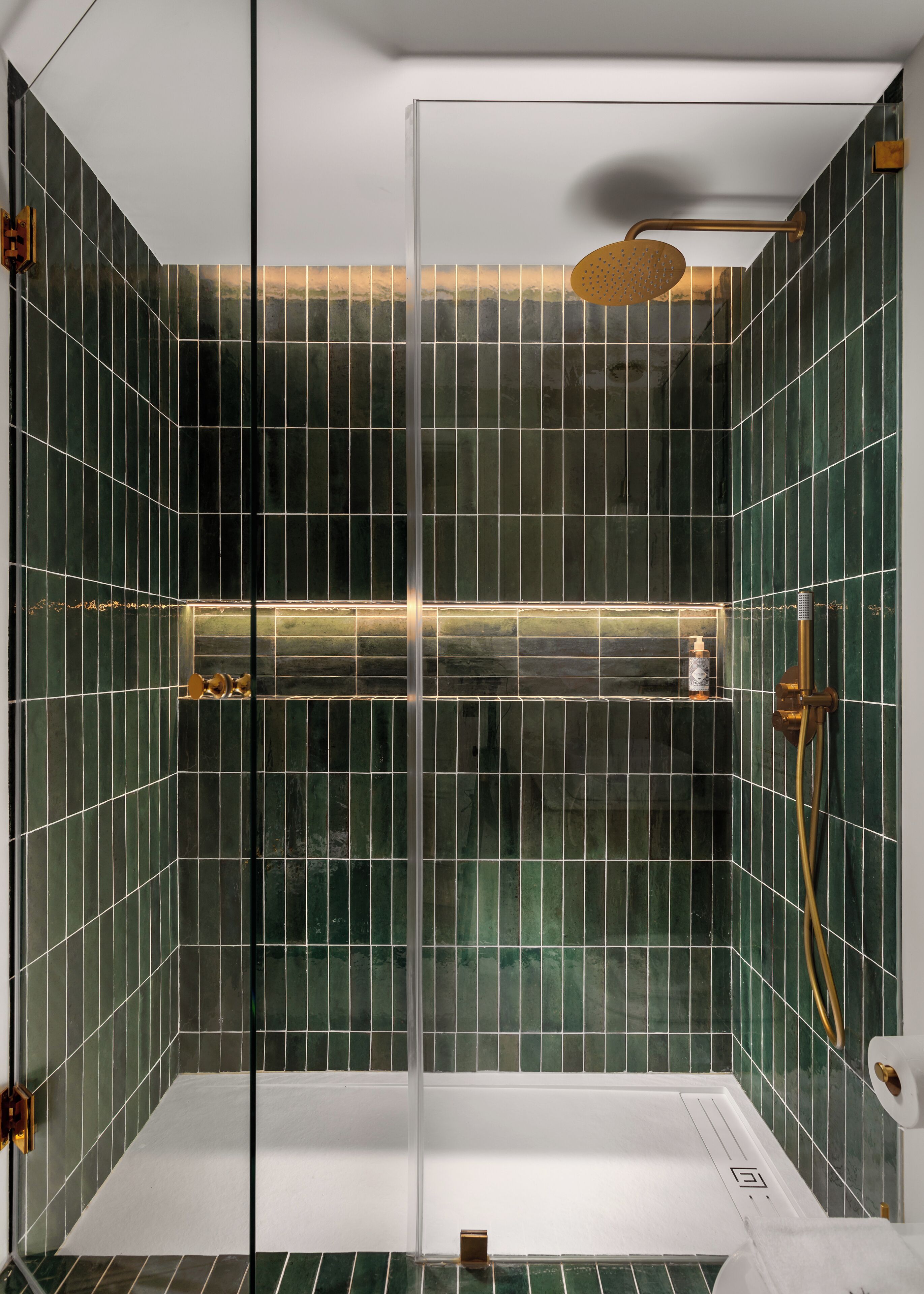 A modern shower with a glass door, green-tiled walls, and a gold showerhead.