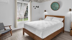 A bedroom with a wooden bed, a window with blinds, a chair, and a wall-mounted light fixture.
