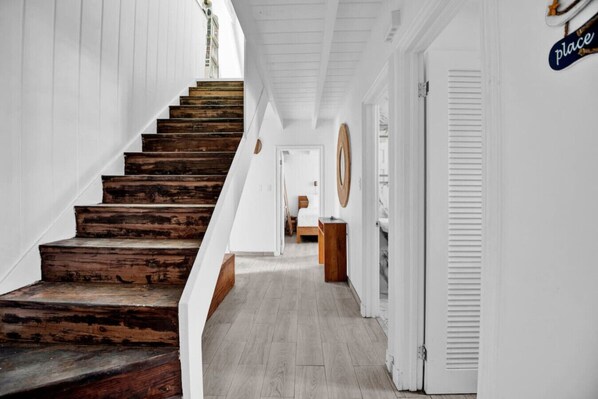 Una escalera de madera conduce a una plataforma, con paredes blancas y un pasillo que tiene una puerta con la etiqueta 'place'.
