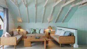 A cozy loft-style room with exposed wooden beams, a sofa set, a coffee table, and a lamp.