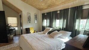 A bedroom with a wooden ceiling, a bed with white bedding, a ceiling fan, and a large window with curtains.