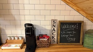 A coffee maker, a basket of snacks, a sign reading "SNACKS", and a chalkboard with "Welcome!" on a kitchen counter.