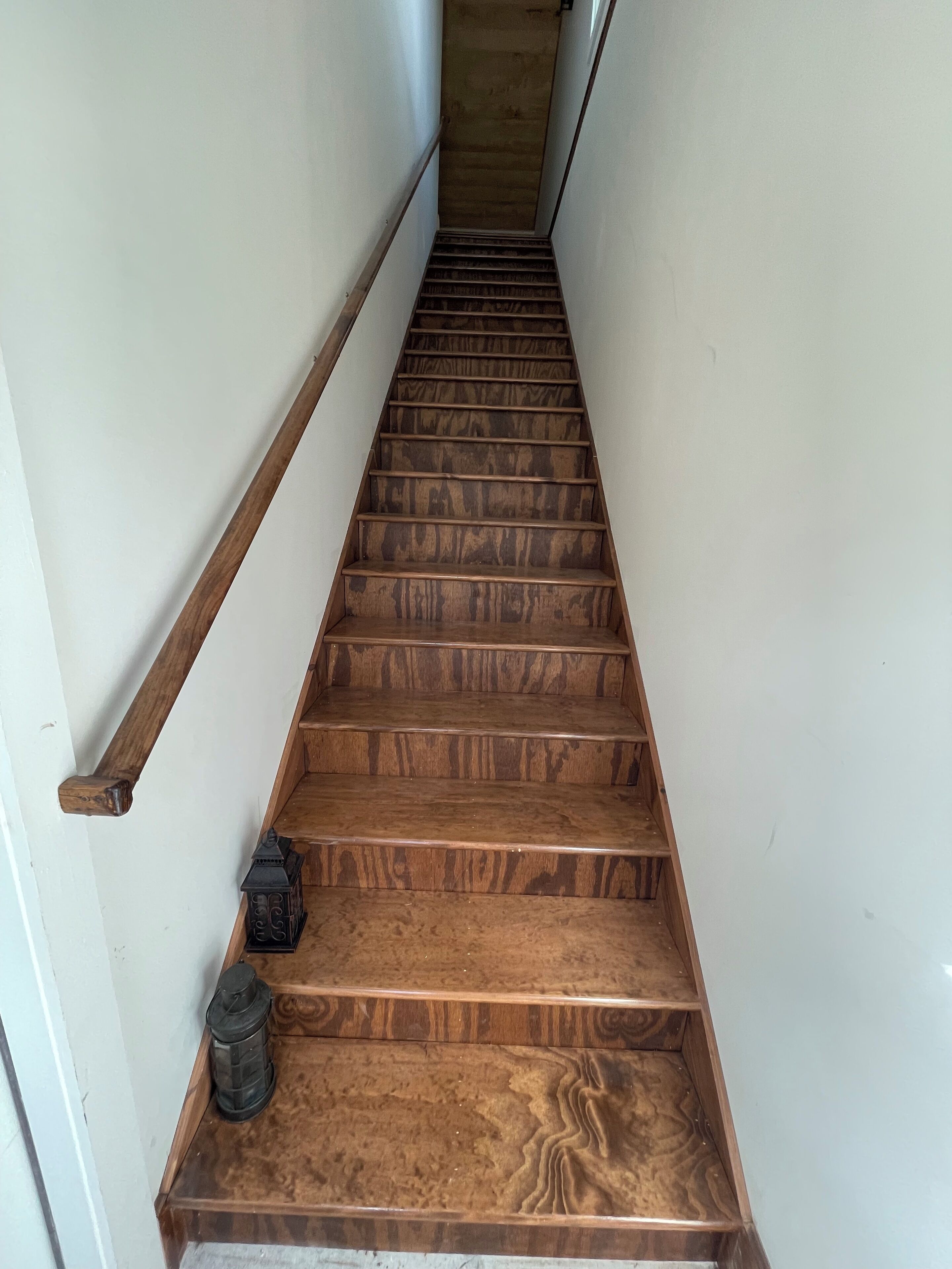 A wooden staircase with a handrail on one side and a lantern on the other.