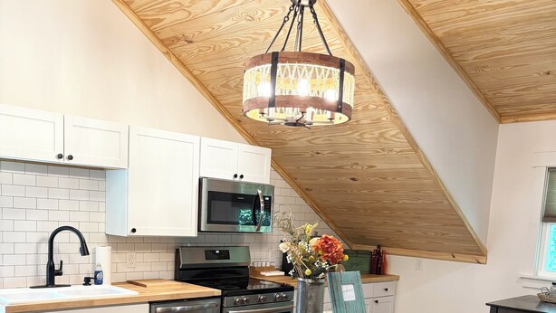 A modern kitchen with white cabinets, a granite countertop, a stainless steel range, and a wooden ceiling.
