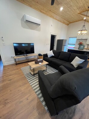 Una sala de estar moderna con un televisor de pantalla plana grande, un sofá negro, una mesa de centro de madera y una alfombra a rayas.