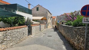 A narrow street with stone walls and a building with a tiled roof. - Amazing apartment in Supetar with lake view (Supetar)