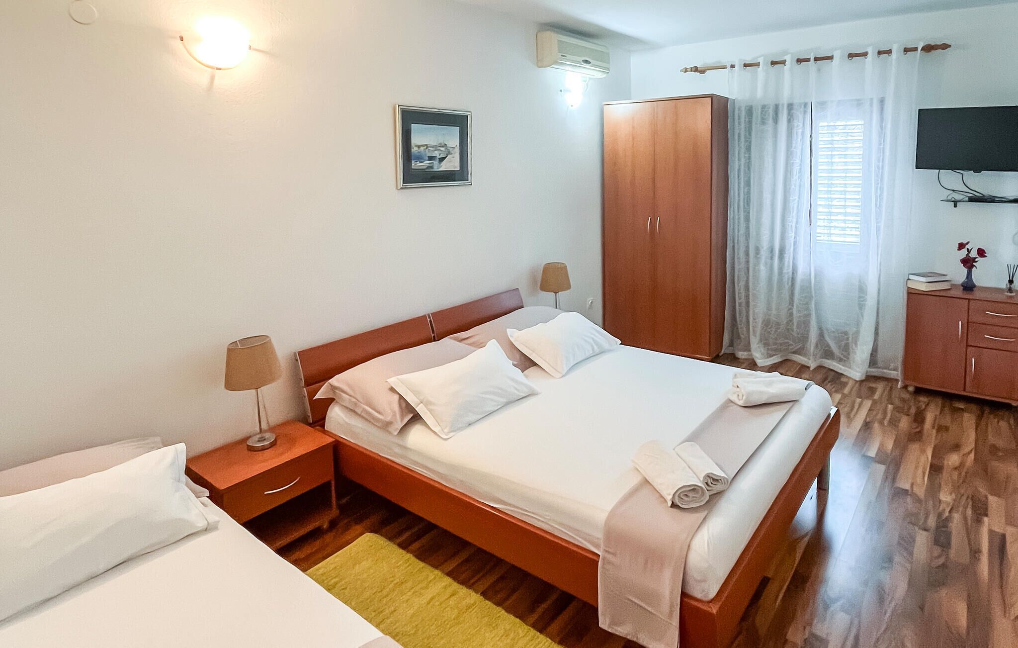 A neatly arranged hotel room with a bed, bedside tables, a wardrobe, a television, and a window with curtains.