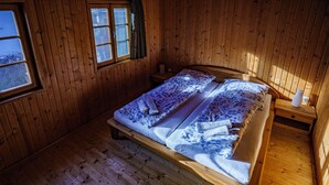 Quarto de cabana de madeira com cama, janela e mesa de cabeceira.
