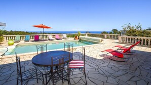 A pool area with lounge chairs and a table, surrounded by stone flooring and a view of the ocean. - Amazing home in Cervione (Cervione)