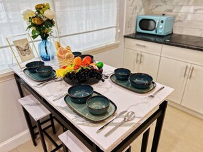A dining table set with bowls and plates, a vase with flowers, and a bowl of fruit. - Ramblei near Chinatown & CenterCity | 1Bedroom-B (Philadelphia)