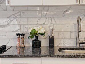 Et køkken med marmorbeklædt bagvæg, en hane i rustfrit stål og en sort vase med hvide blomster.