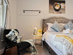 Une chambre à coucher comprenant un lit, une chaise, une petite table avec une lampe et une étagère fixée au mur.