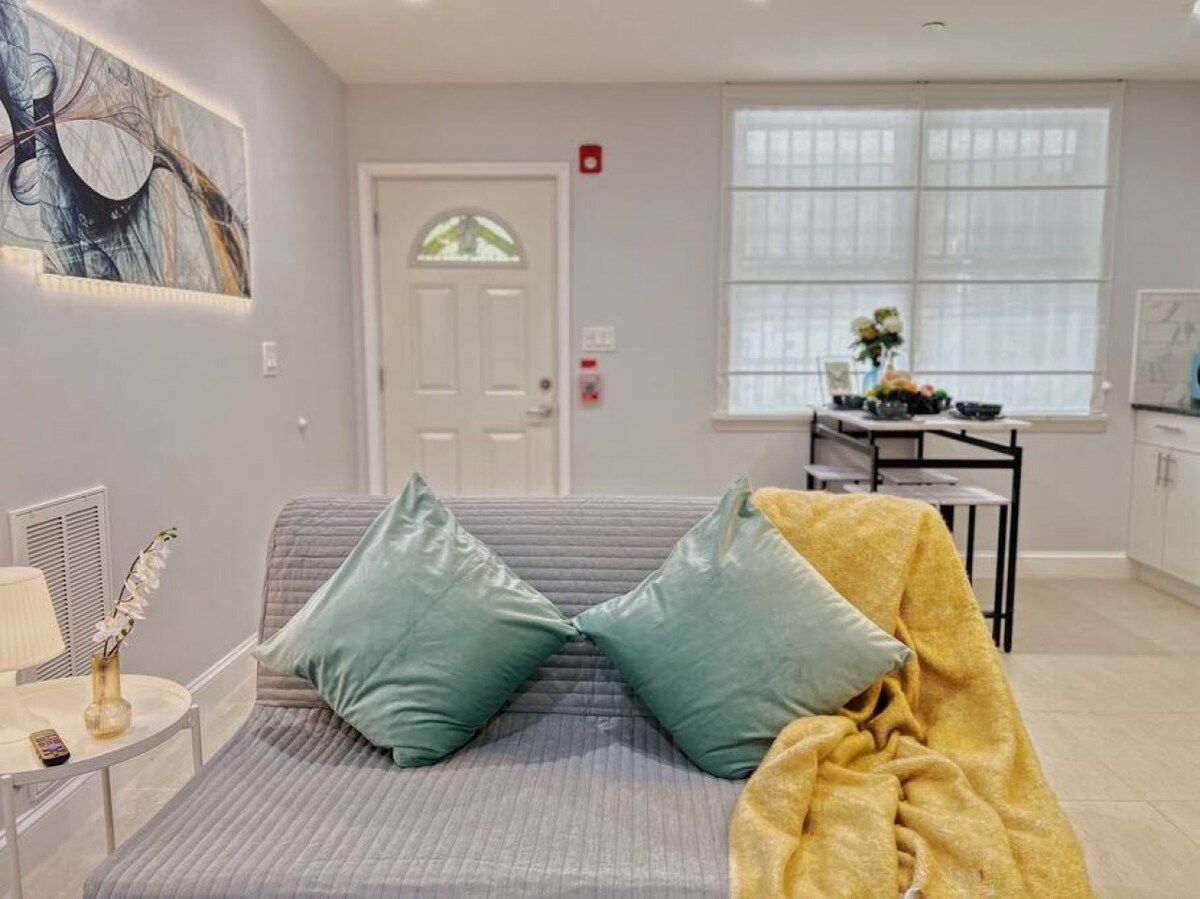 Una sala de estar moderna con un sofá, almohadones, una mesa con una lámpara y un cuadro en la pared.