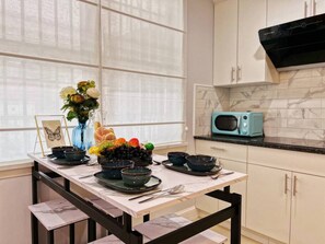 Une cuisine dotée d’un plan de travail en marbre, d’un micro-ondes de couleur turquoise et d’une table à manger mise avec des bols et des assiettes.