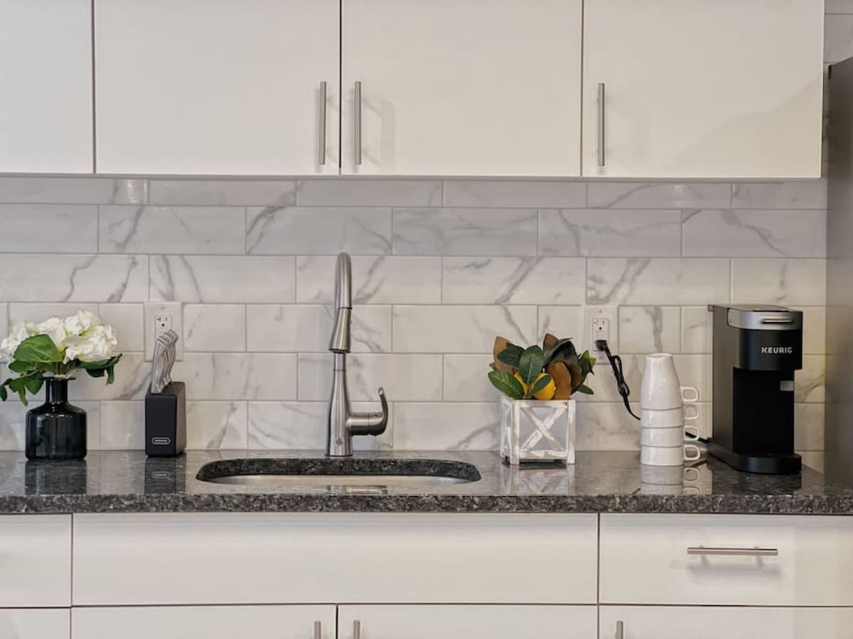 A kitchen with a marble backsplash, a stainless steel faucet, a coffee maker, and a vase with flowers.