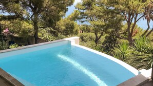 A rectangular swimming pool with clear blue water, surrounded by lush greenery and trees, with a view of the sea in the background. - Beautiful home in Sète (Sète)