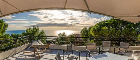 A covered outdoor seating area with a view of the sea and trees.