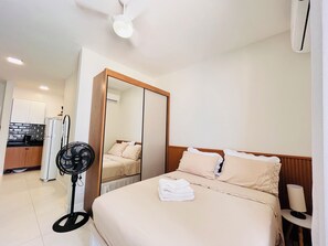A hotel room with a bed, a bedside table, a fan, a mirror, a wardrobe, and a kitchenette. - Toque a Campainha 207 Vendaval (Cabo Frio)