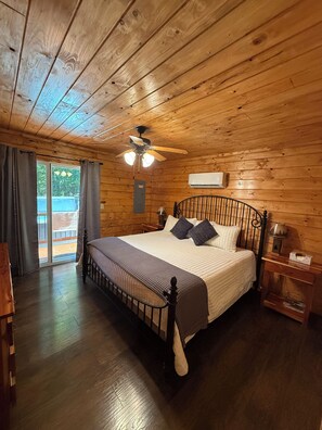 A wooden cabin bedroom with a bed, a ceiling fan, and a window with curtains.
