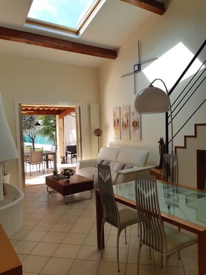 A spacious living area with a glass dining table, a white sofa, and a staircase. - House with swimming pool in a village between Cannes and Grasse on the mimosa road (Pégomas)