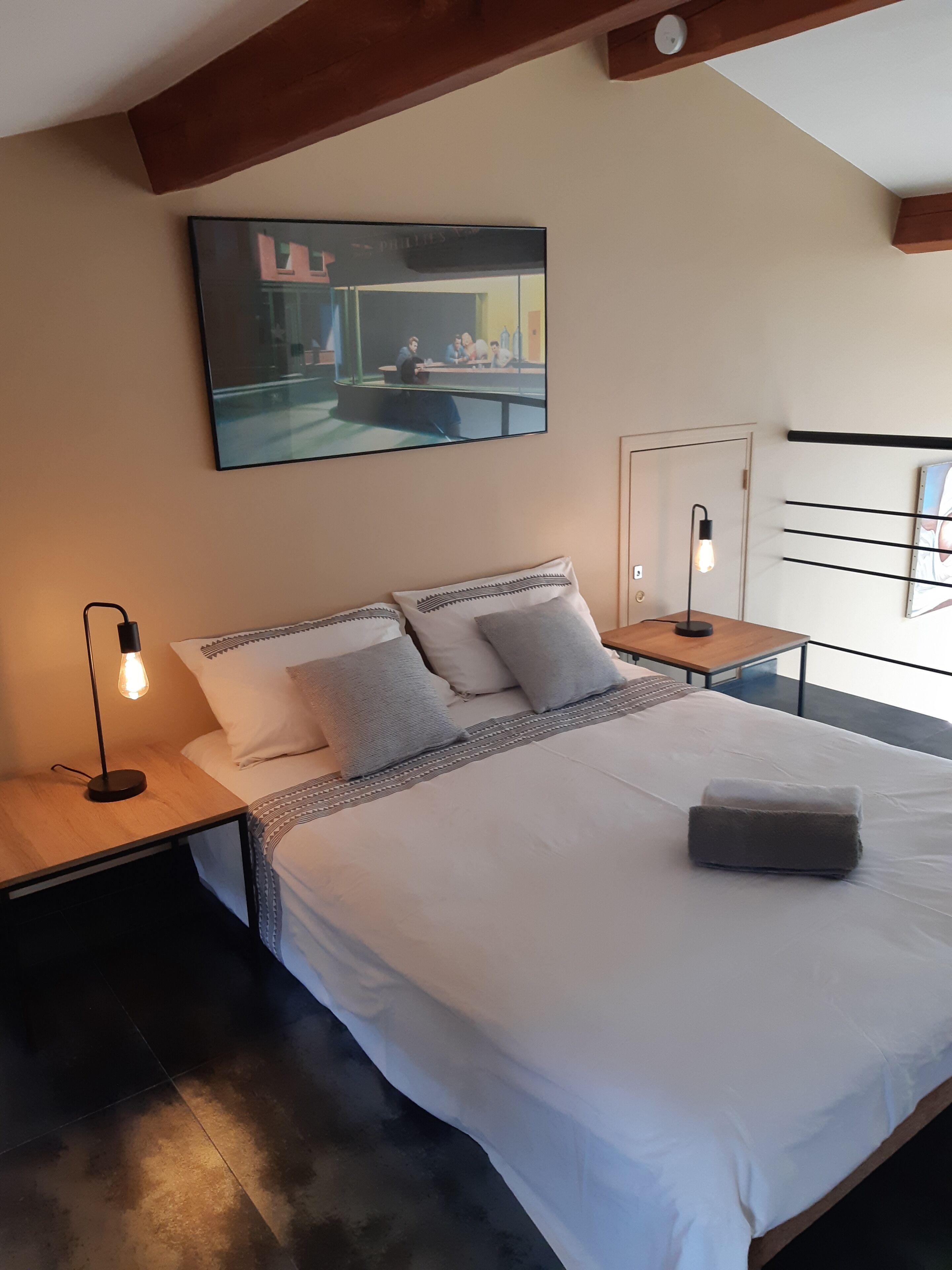 Een slaapkamer met een bed, nachtkastjes, een lamp, een schilderij en een raam.