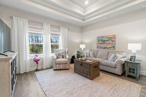 A living room with a sofa, armchair, and a coffee table. There is a window with curtains, a lamp, and a painting on the wall.
