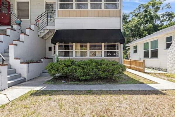 A two-story building with a black awning, a small garden, and a staircase leading to an upper level.