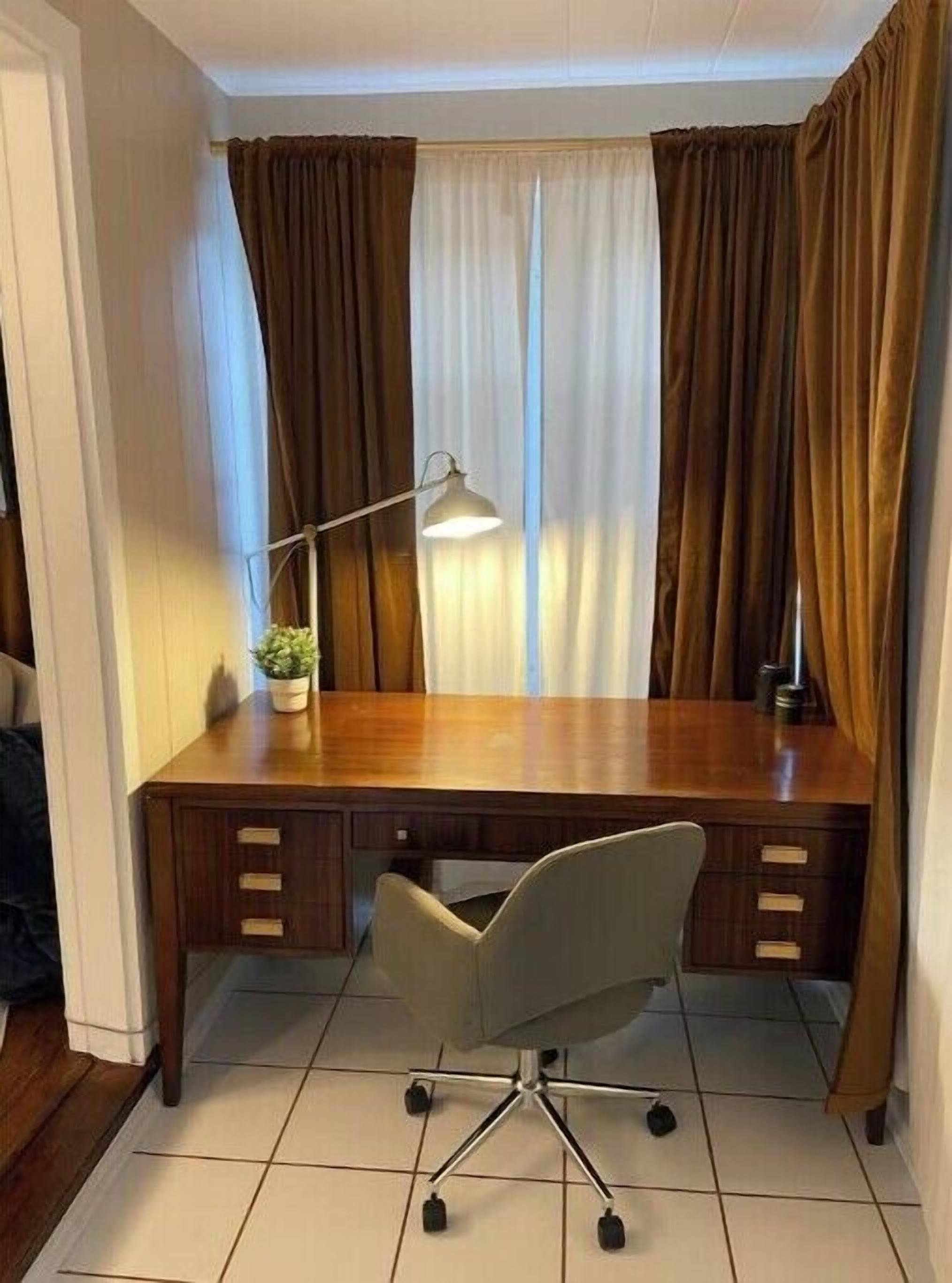 A wooden desk with a chair, a lamp, and a plant.