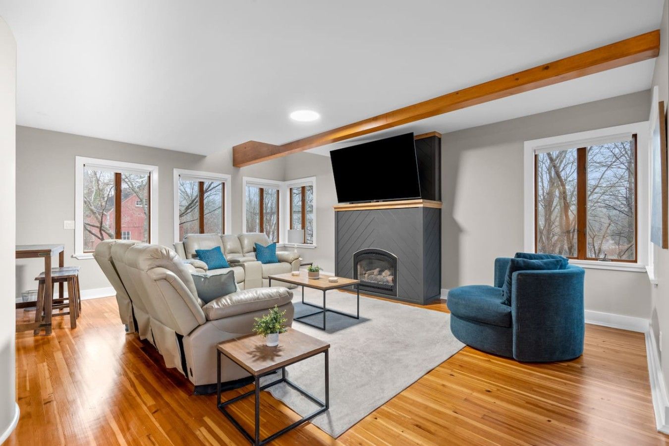 A modern living room with a fireplace, leather sofas, a flat-screen TV, and large windows.