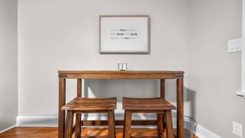 A room with a wooden table and two matching chairs, a framed quote on the wall, and a light switch on the wall.