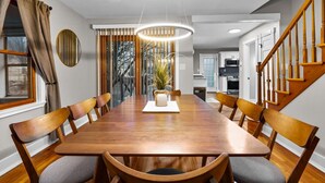 A dining room with a long wooden table, six chairs, a chandelier, and a view of a kitchen and staircase. - #30 - Spacious & Cozy! (Southington)