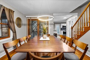 A dining room with a long wooden table, six chairs, a chandelier, and a view of the outdoors through large windows. - #30 - Spacious & Cozy! (Southington)