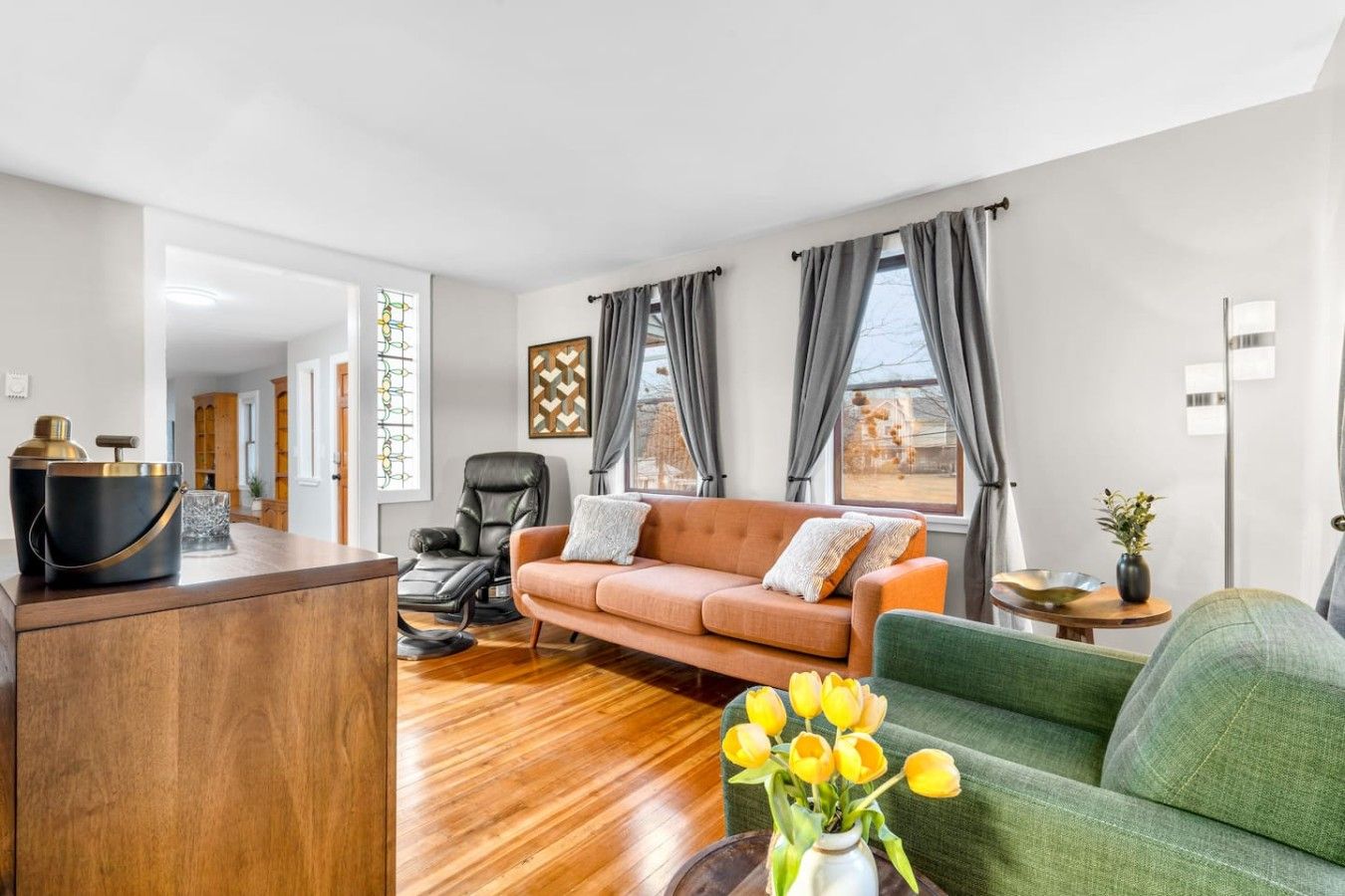 Una sala moderna con un sofá, un sillón verde y una mesa de centro de madera. Hay una silla y una mesita con un jarrón de flores.