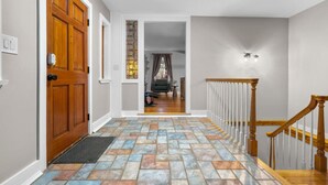 A hallway with a wooden door, a glass door with a colorful pattern, a staircase with wooden railings, and a patterned tile floor. - #30 - Spacious & Cozy! (Southington)