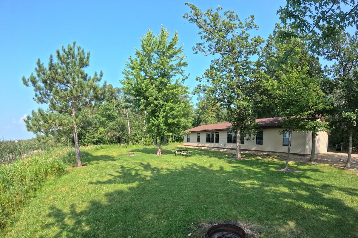 Une maison avec un toit rouge, entourée d’une cour verdoyante et d’arbres.