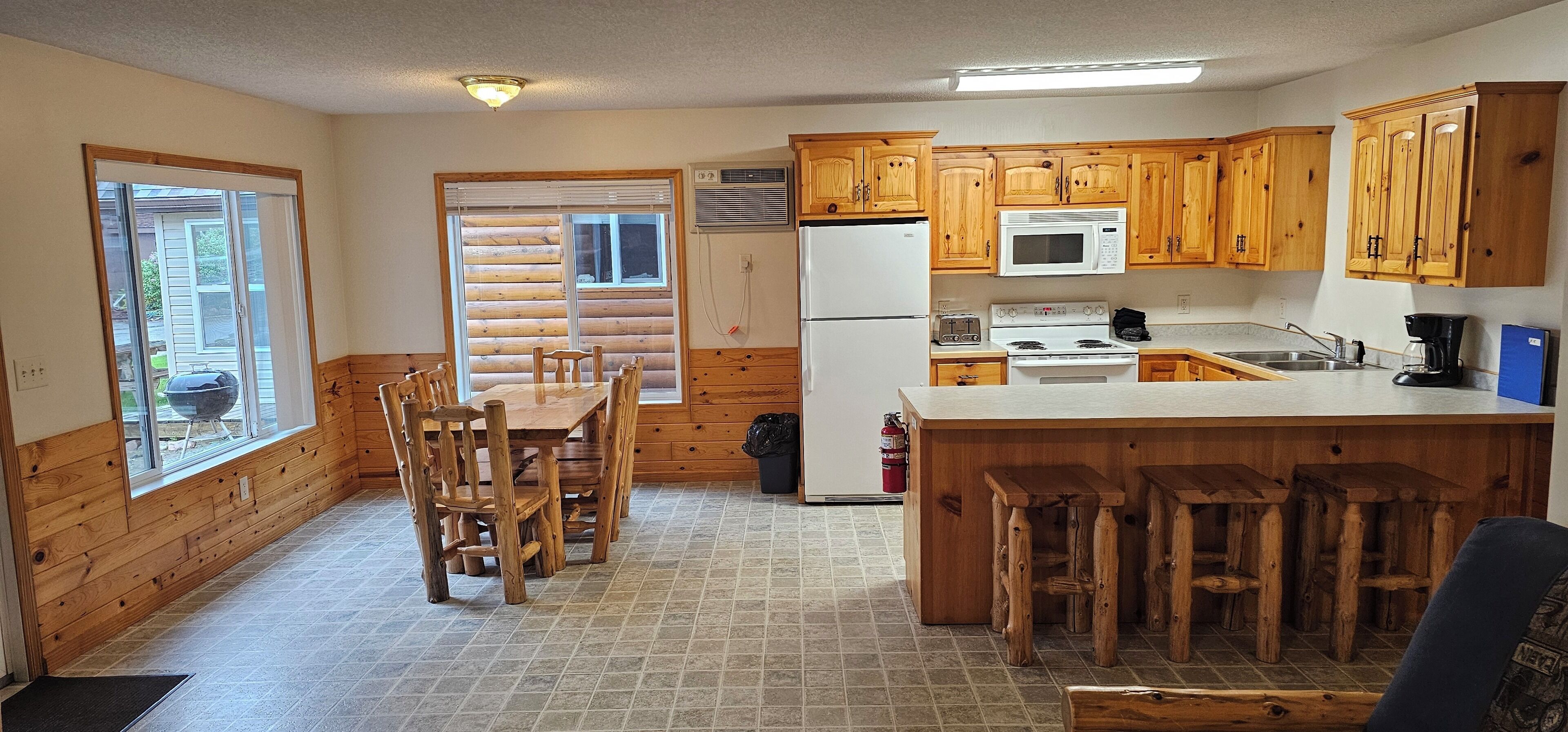 A kitchen with wooden cabinets, a refrigerator, a microwave, a stove, and a dining area with chairs and a table.