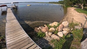 Un muelle de madera se extiende sobre aguas tranquilas, con barcos y un parque infantil cerca.