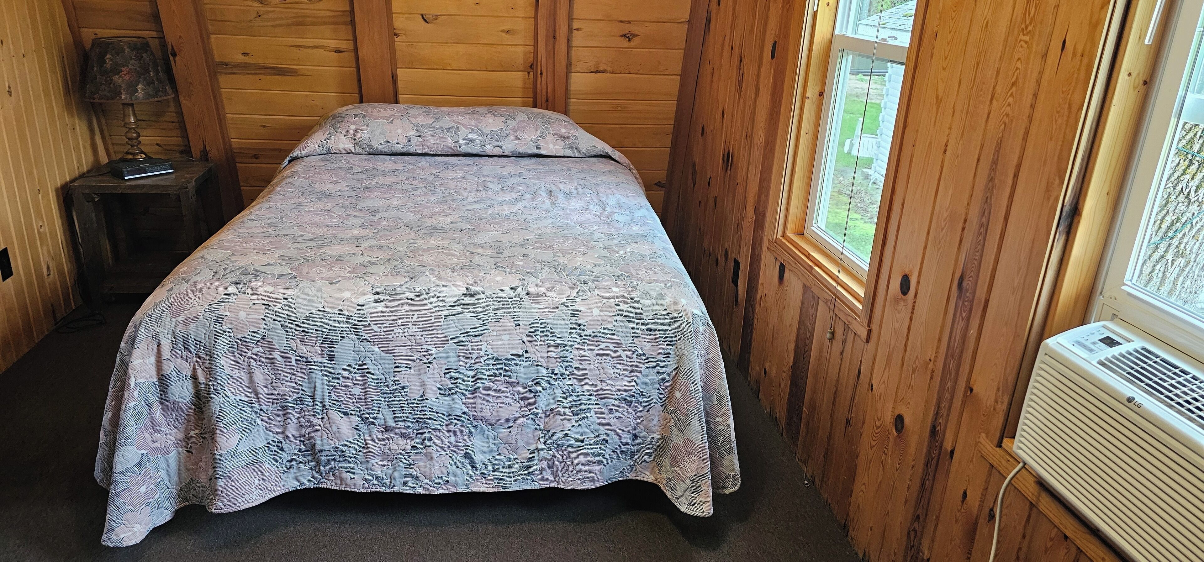Una stanza in legno con un letto, una lampada e una finestra.