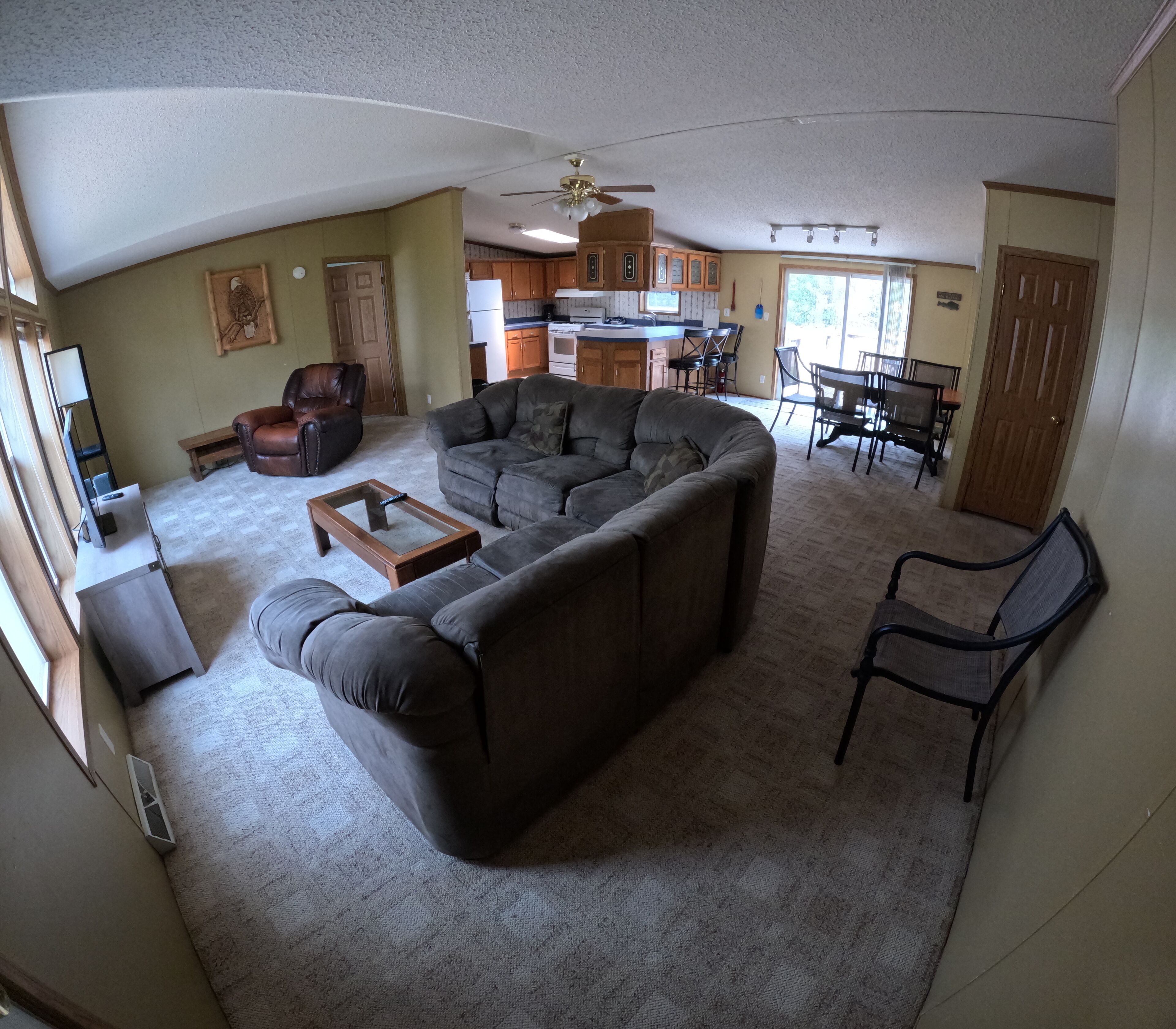 A living room with a large sectional sofa, a coffee table, and a TV stand. There is a dining area with a table and chairs, and a kitchen in the background.
