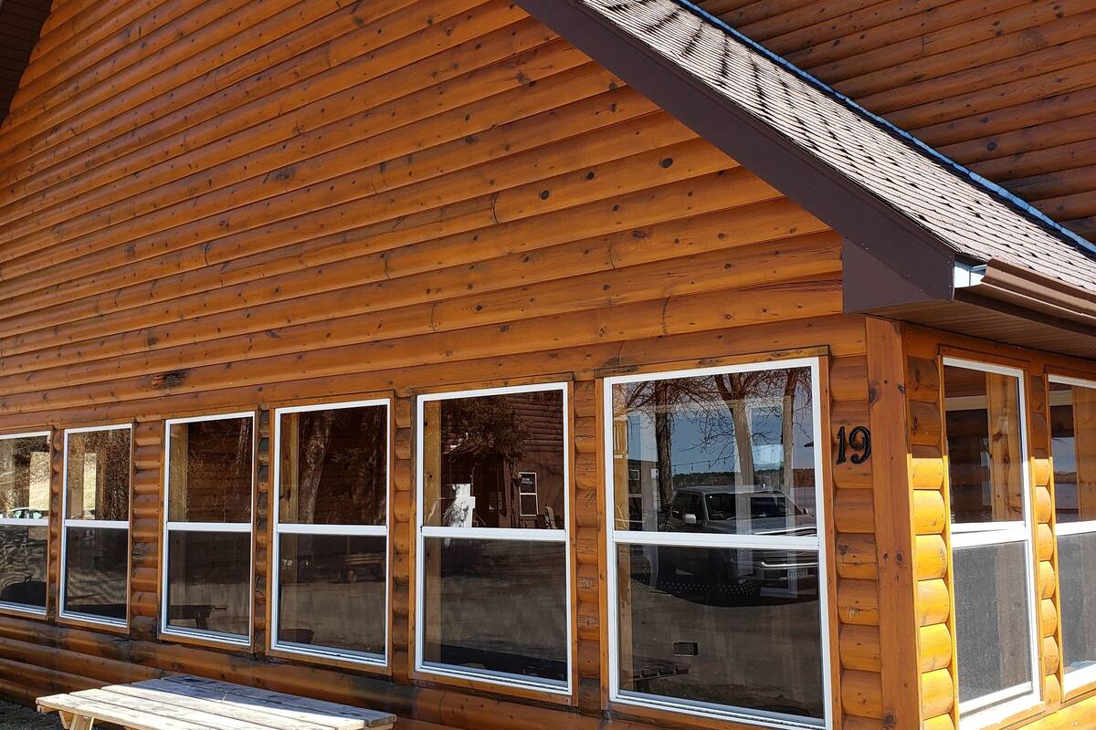 Une cabane en rondins dotée de grandes fenêtres et d’une table de pique-nique à l’extérieur.