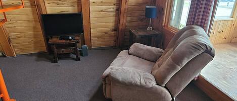 A cozy room with a wooden interior, a brown sofa, a television on a wooden stand, and a lamp on a small table.