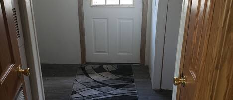 A hallway with a wooden door, a patterned rug, and a view of the outside.