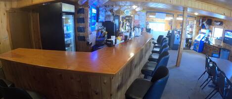 Un espace bar avec un comptoir en bois, des tabourets de bar noirs et un panneau lumineux au néon.