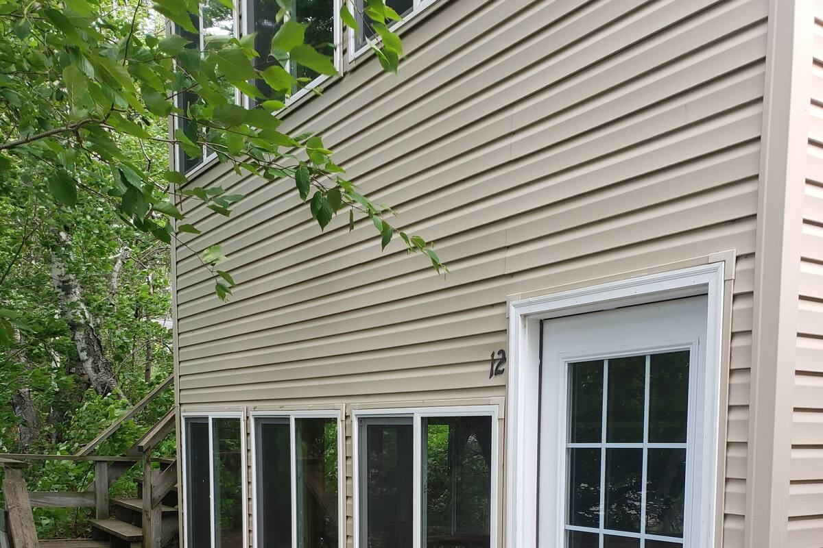Une maison avec une terrasse en bois, une porte blanche et de nombreuses fenêtres.
