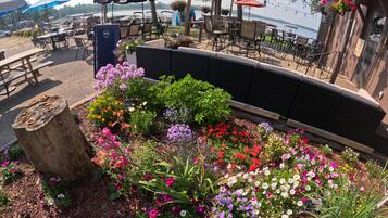 Zona salotto all'aperto con tavoli e sedie, circondata da un'aiuola con fiori colorati di ogni tipo.